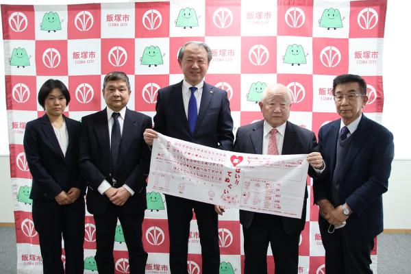 手ぬぐいを持って記念写真に写る飯塚市ボランティア連絡協議会の皆様と武井市長