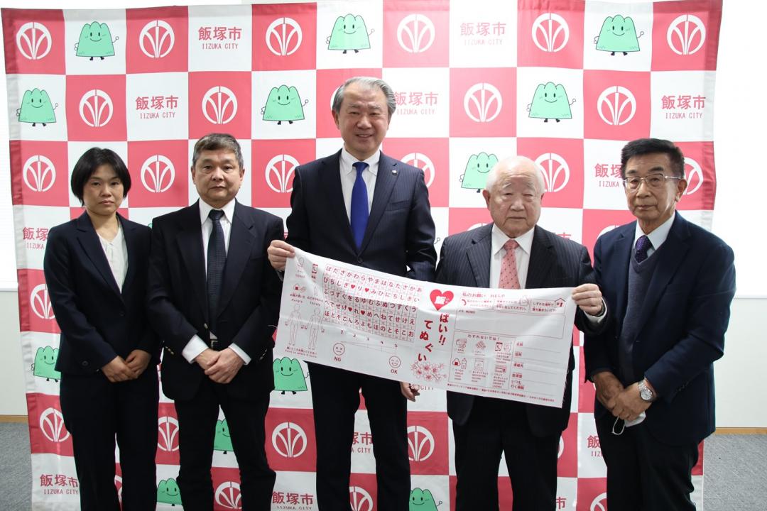 手ぬぐいを持って記念写真に写る飯塚市ボランティア連絡協議会の皆様と武井市長