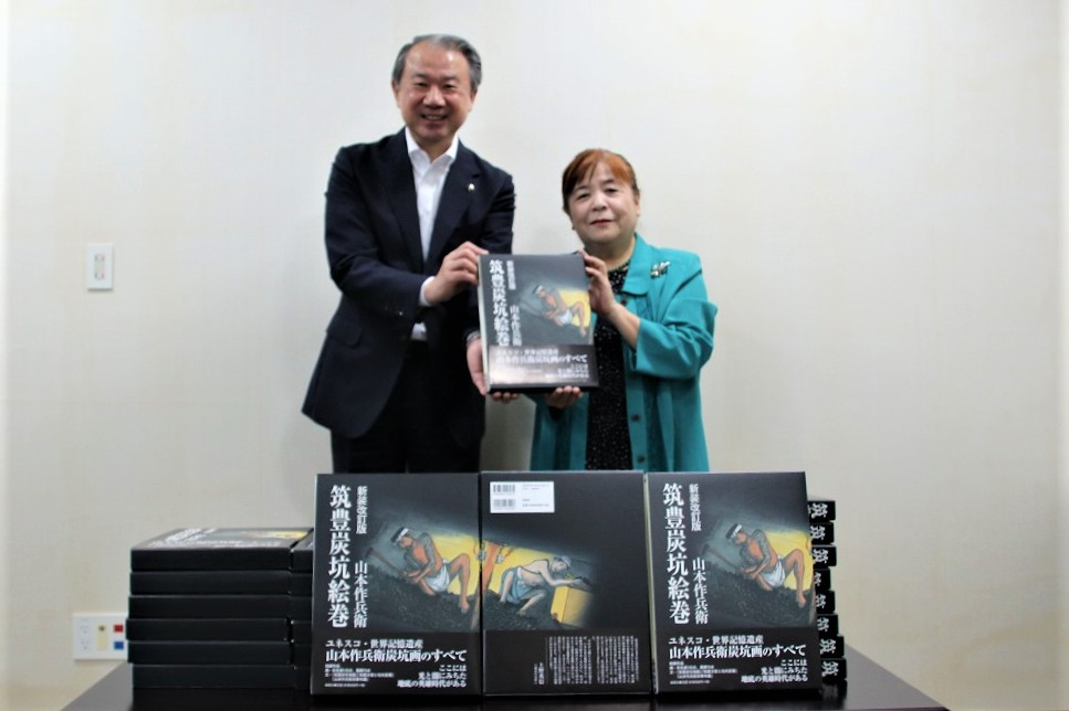 市長と一緒に山本作兵衛氏の書籍を持つ寄贈者の緒方さん